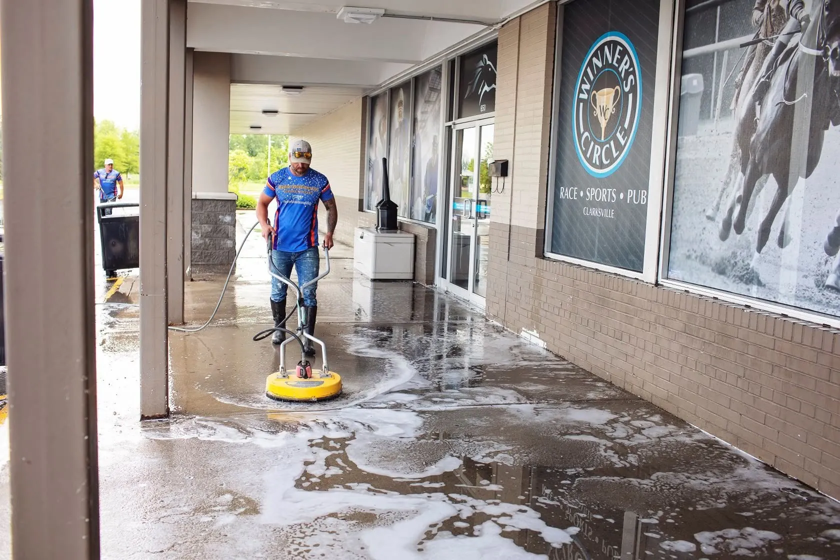Worker surface cleaning a soapy covered walkway in front of a storefront