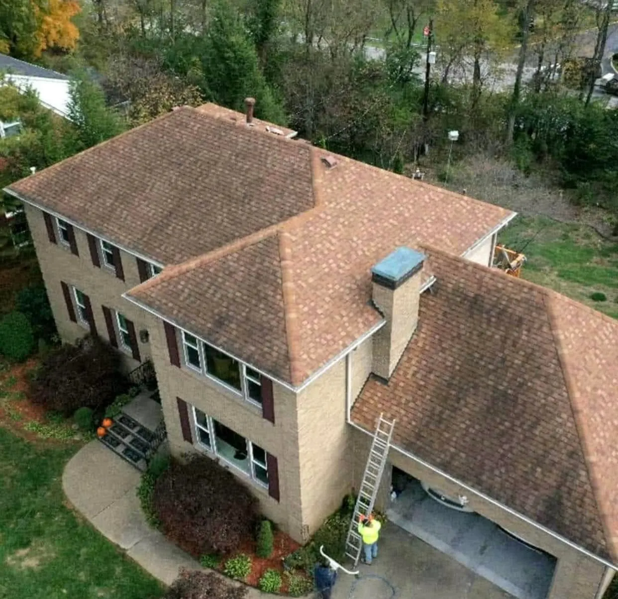 Aerial view of a two-story house with a worker on a ladder beside the garage