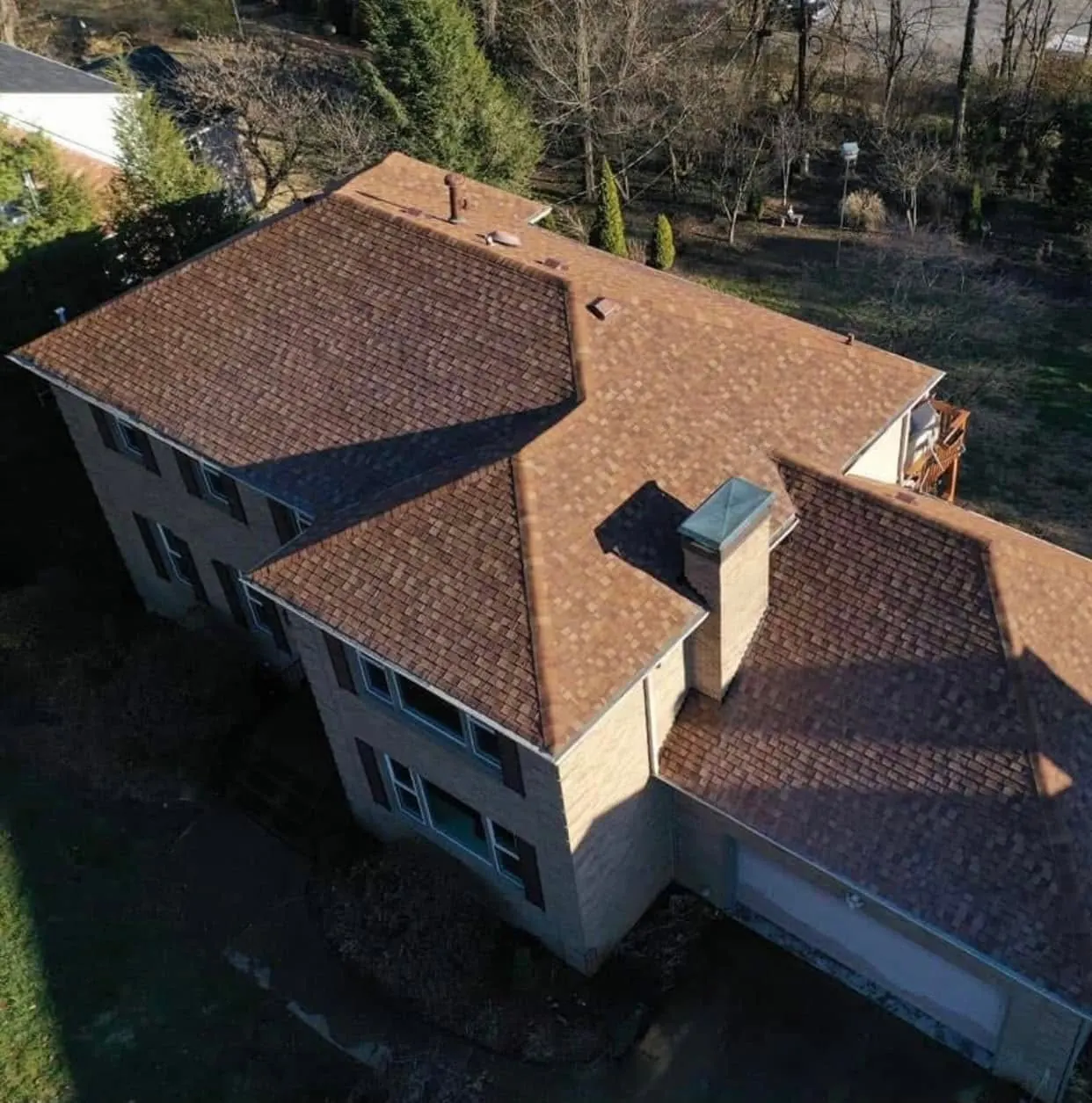 Aerial view of a two-story house with a brown shingle roof and light siding