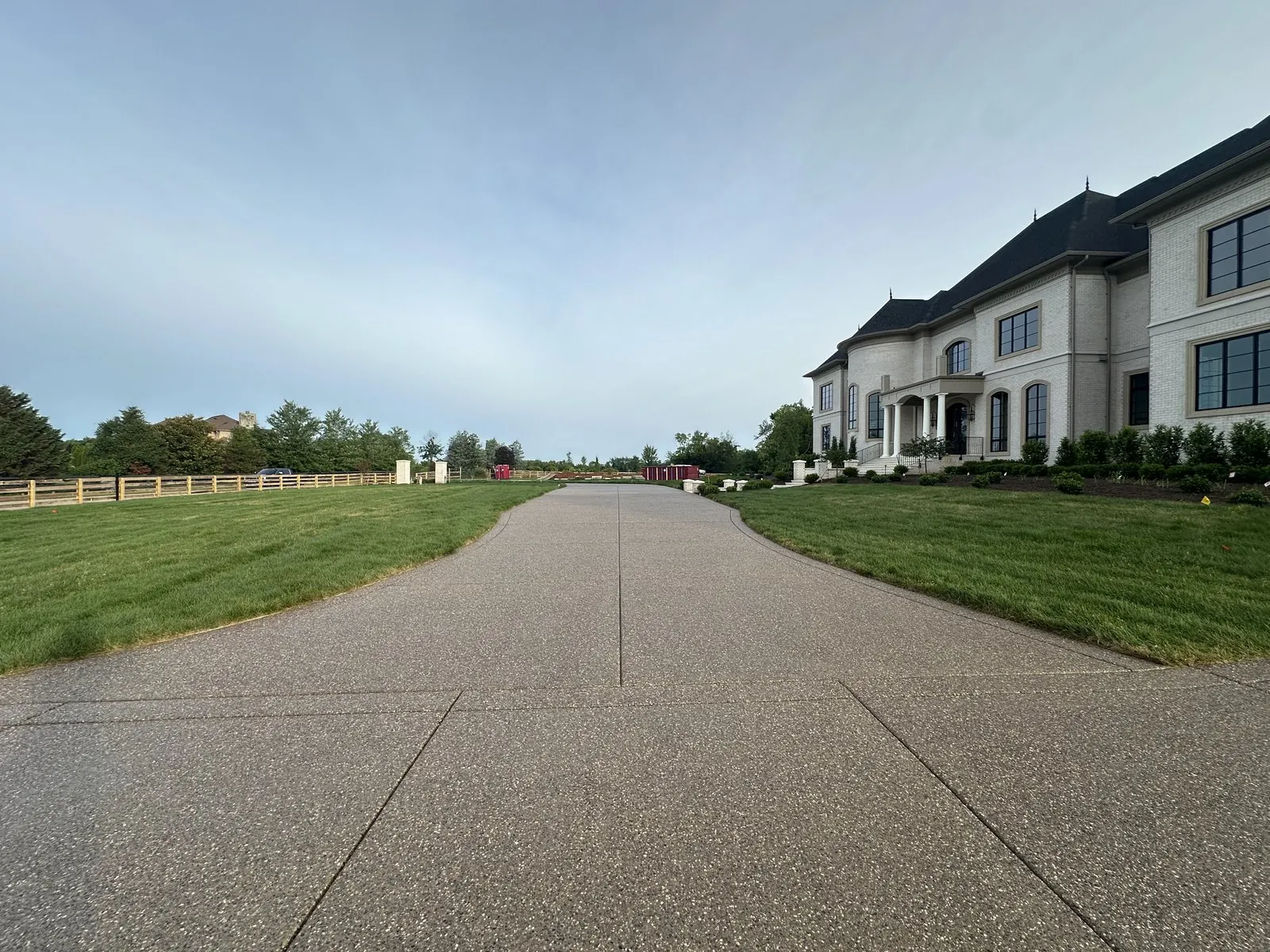 Long exposed-aggregate concrete driveway leading to a large white home