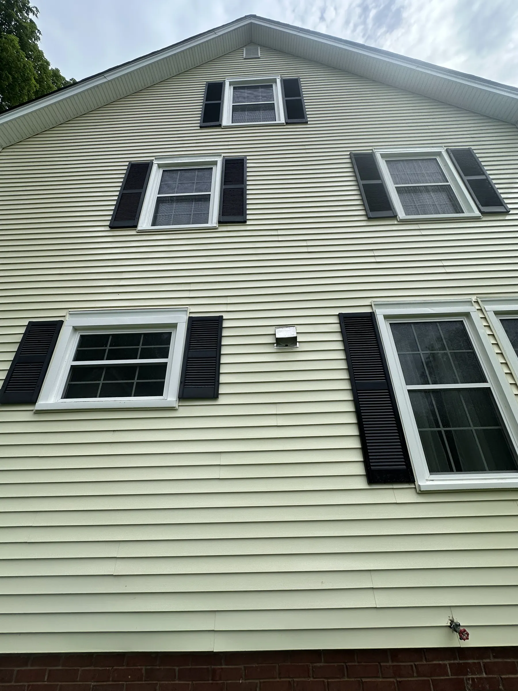 Clean yellow siding and white trim on a house gable after washing