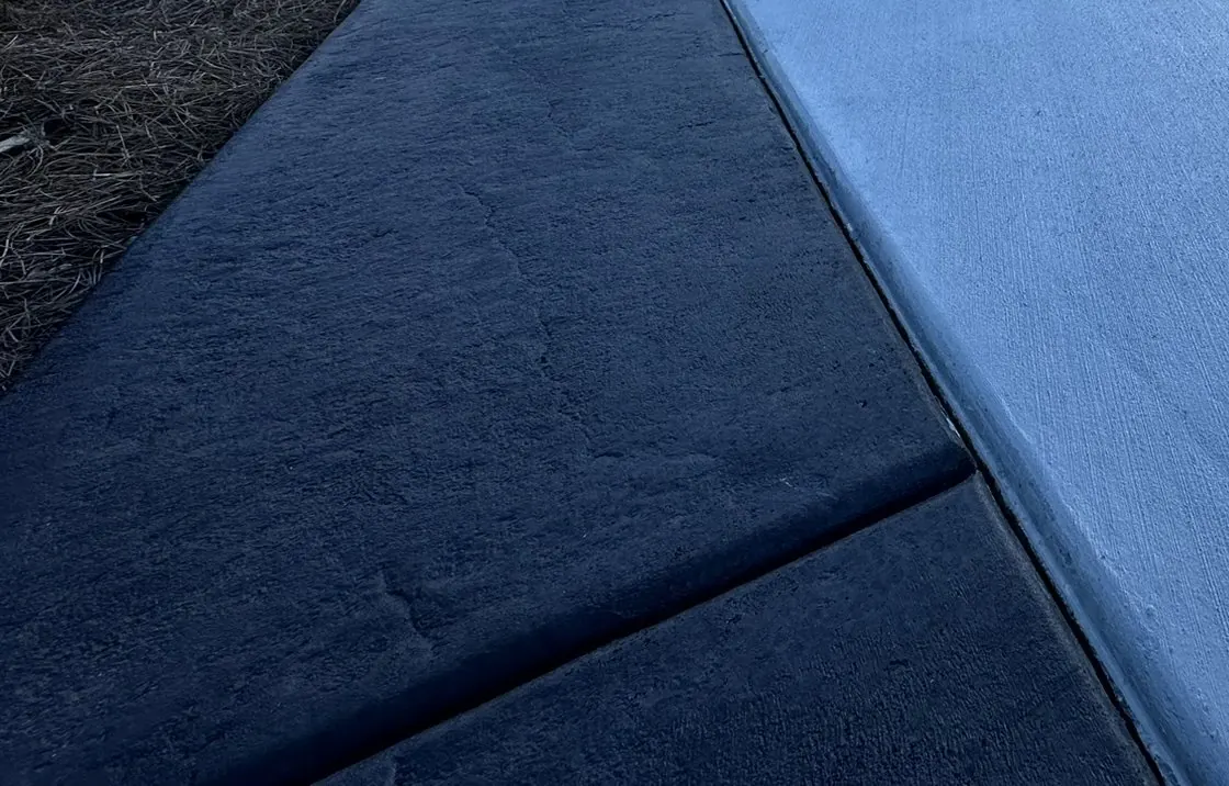 Close view of a dark stamped-concrete border along a broom-finish driveway