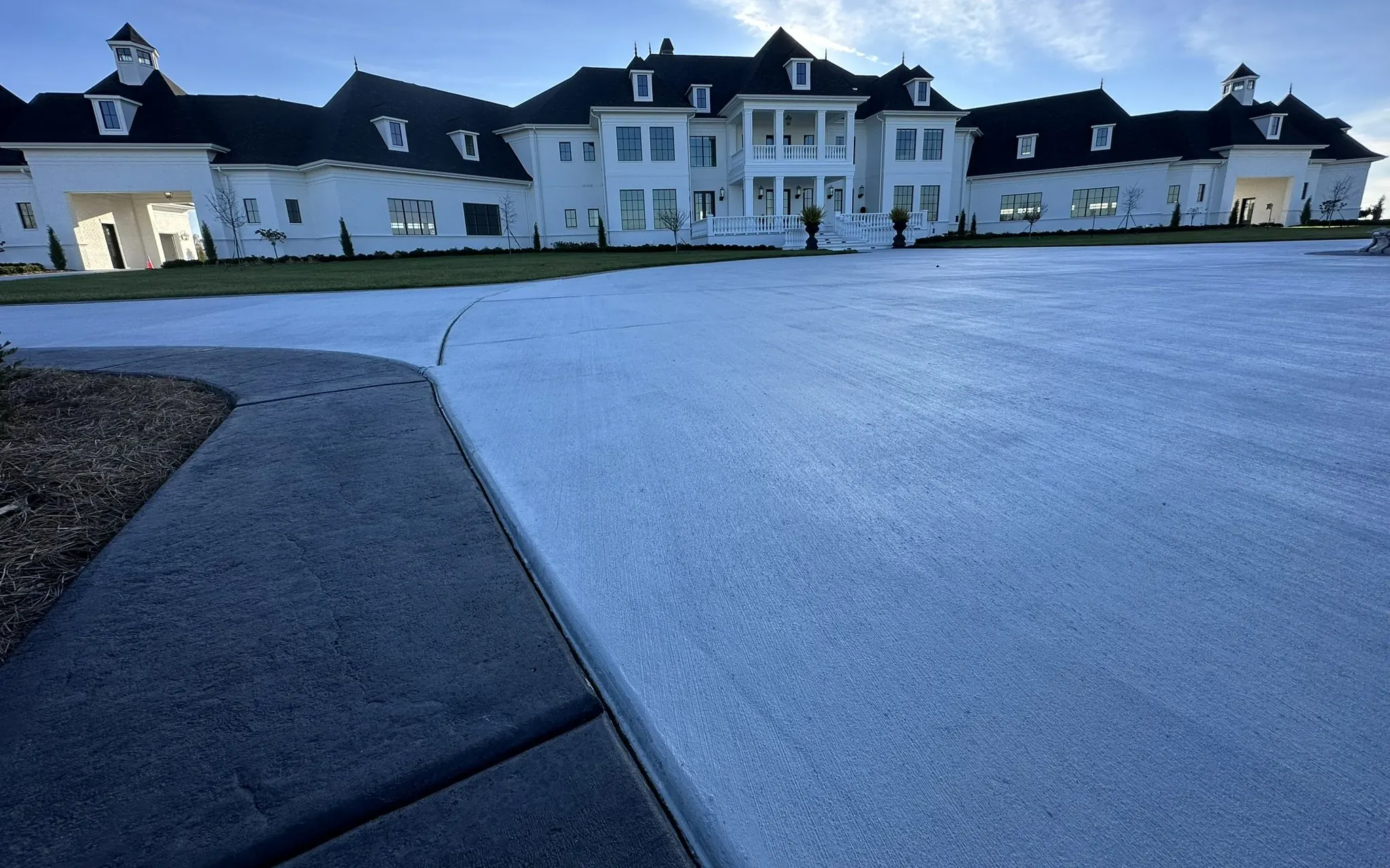 Wide broom-finish concrete driveway with a dark stamped-concrete border in front of a large white home