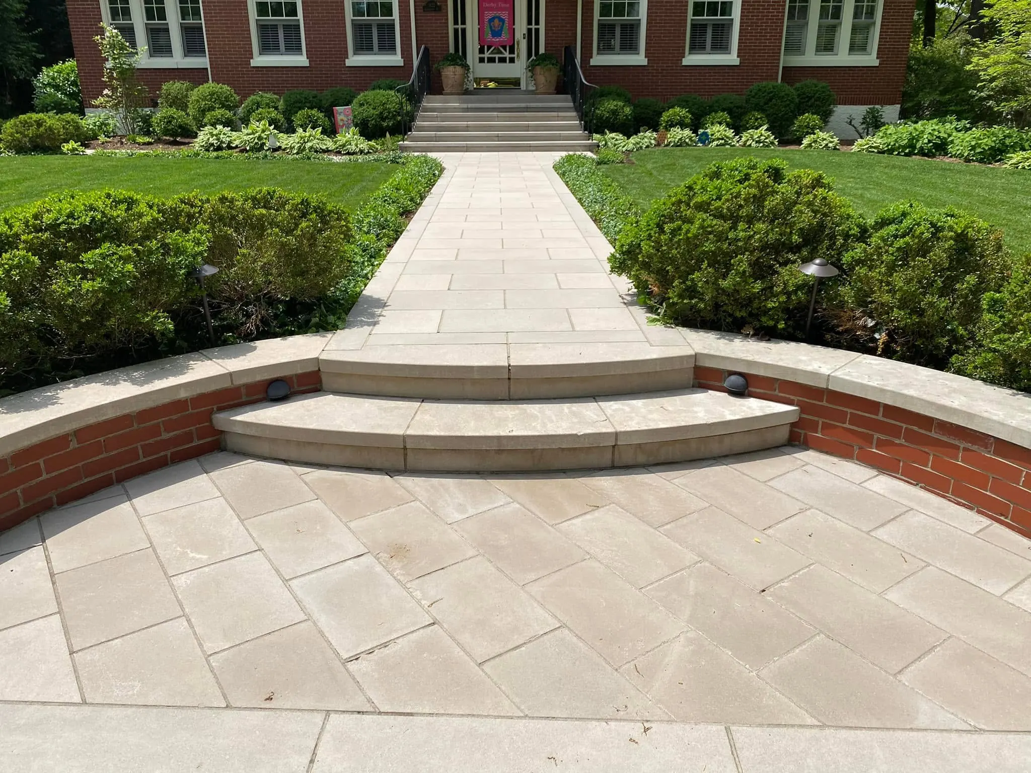 Clean stone patio, curved steps and walkway in front of a brick home