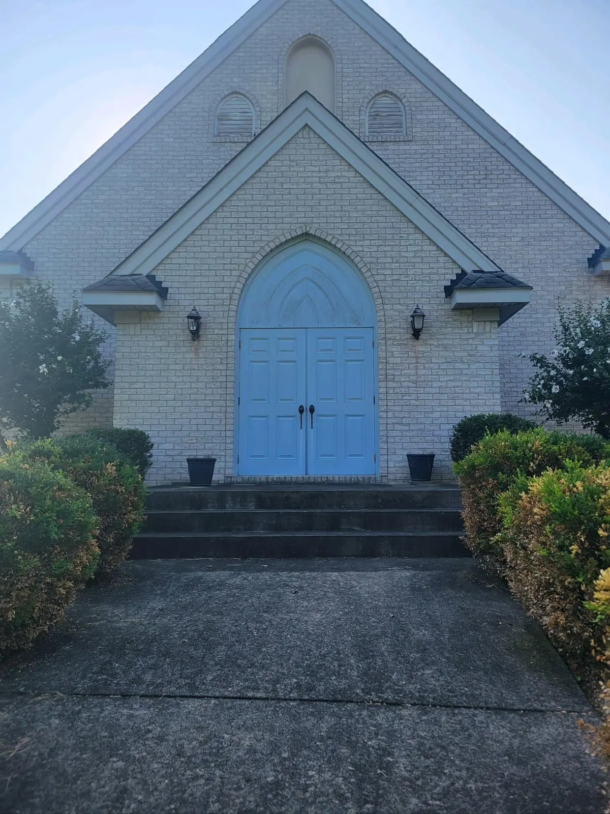 Painted brick church entrance with blue arched doors and steps, before cleaning