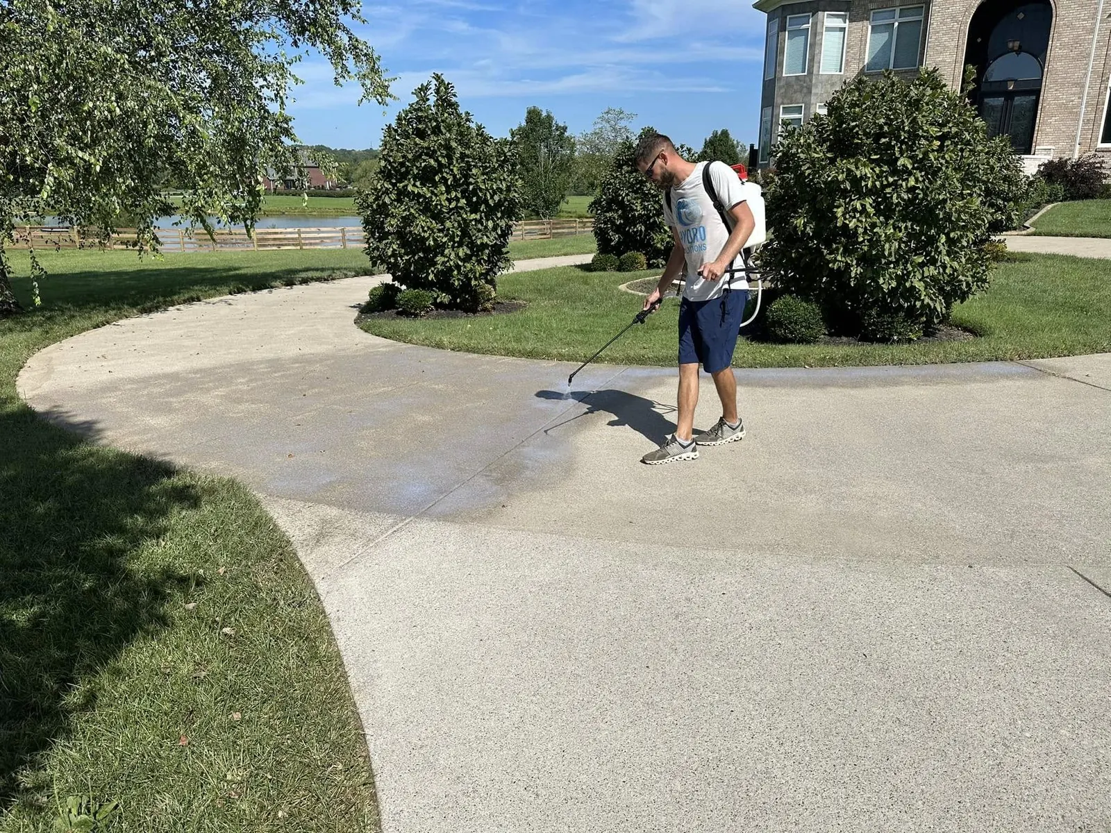 Worker applying sealer to a curved concrete walkway beside a lawn