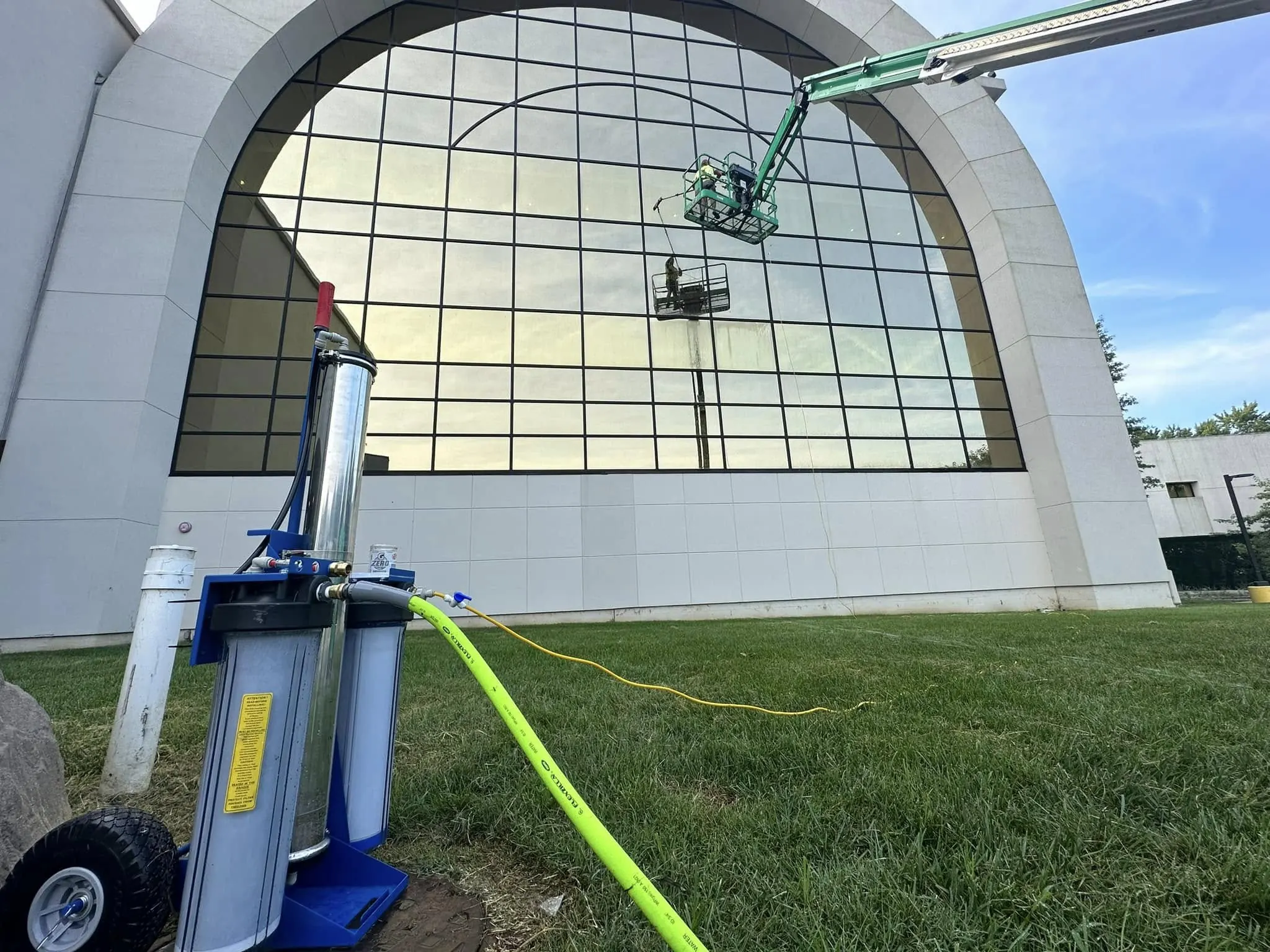 Water-fed filtration cart in front of a large glass building, with a boom lift at the facade