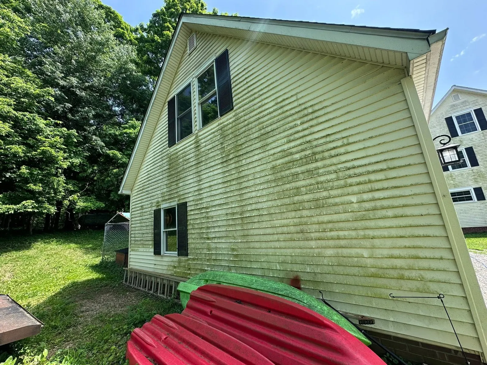 Yellow vinyl siding on the gable end of a house, streaked with green mildew, kayaks on the lawn