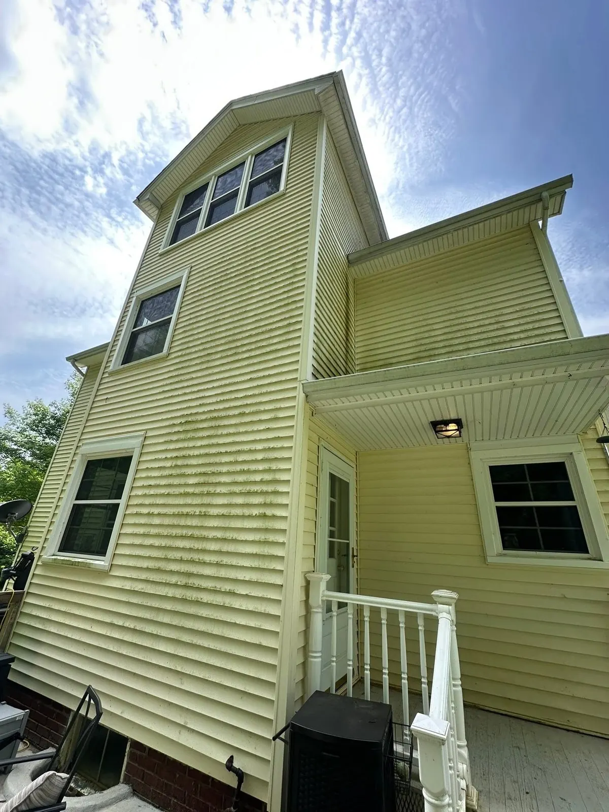 Back of a yellow house with green mildew on the siding