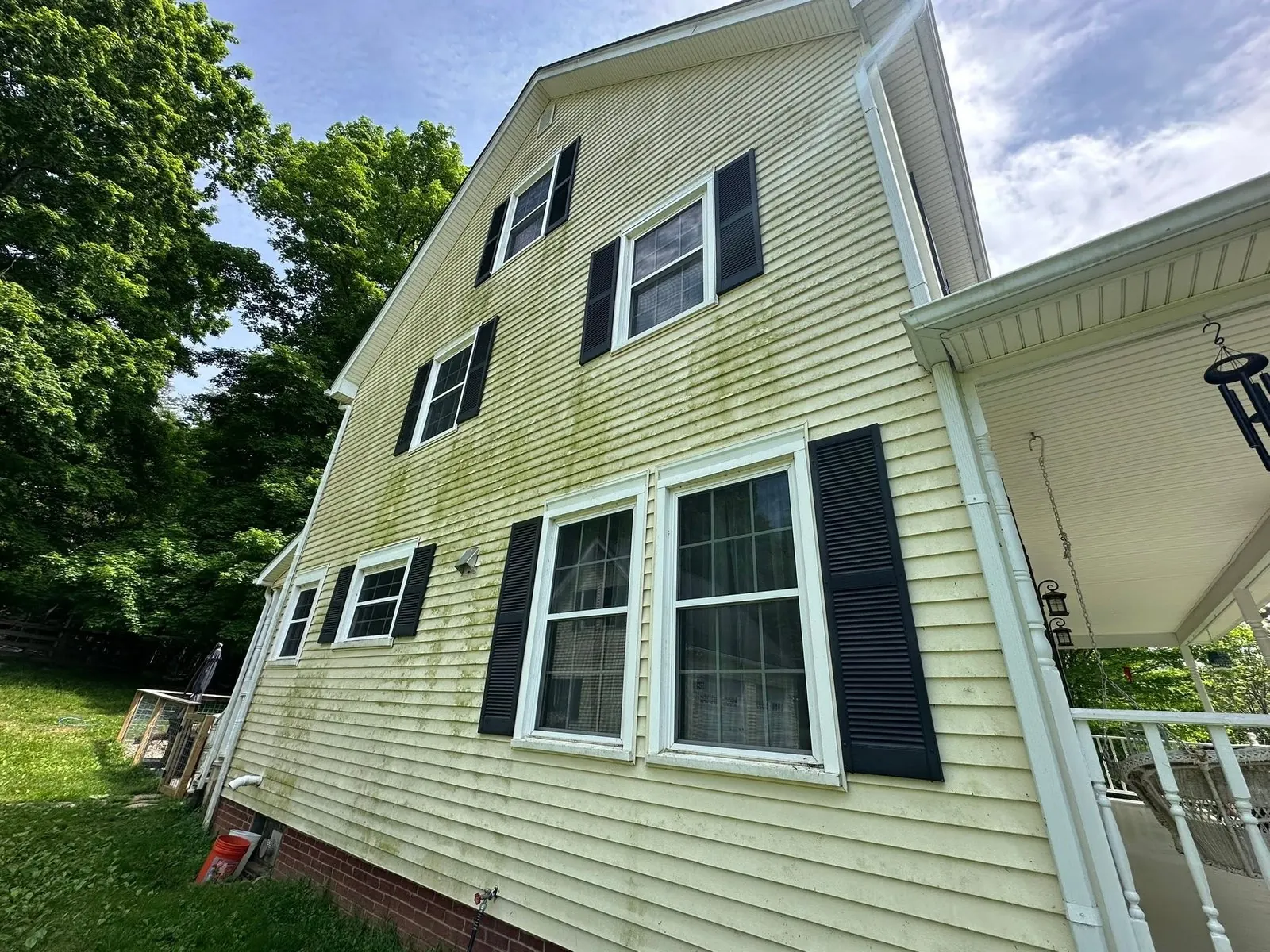 Side of a yellow house with black shutters and heavy green mildew streaks