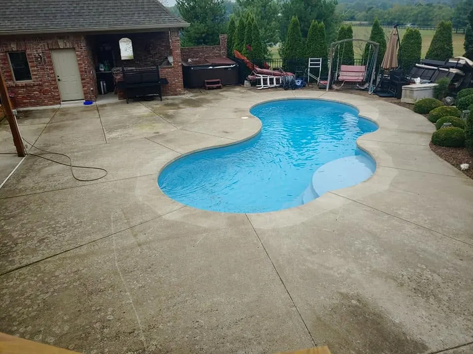 Stained concrete pool deck around a kidney-shaped pool, with a hose on the deck