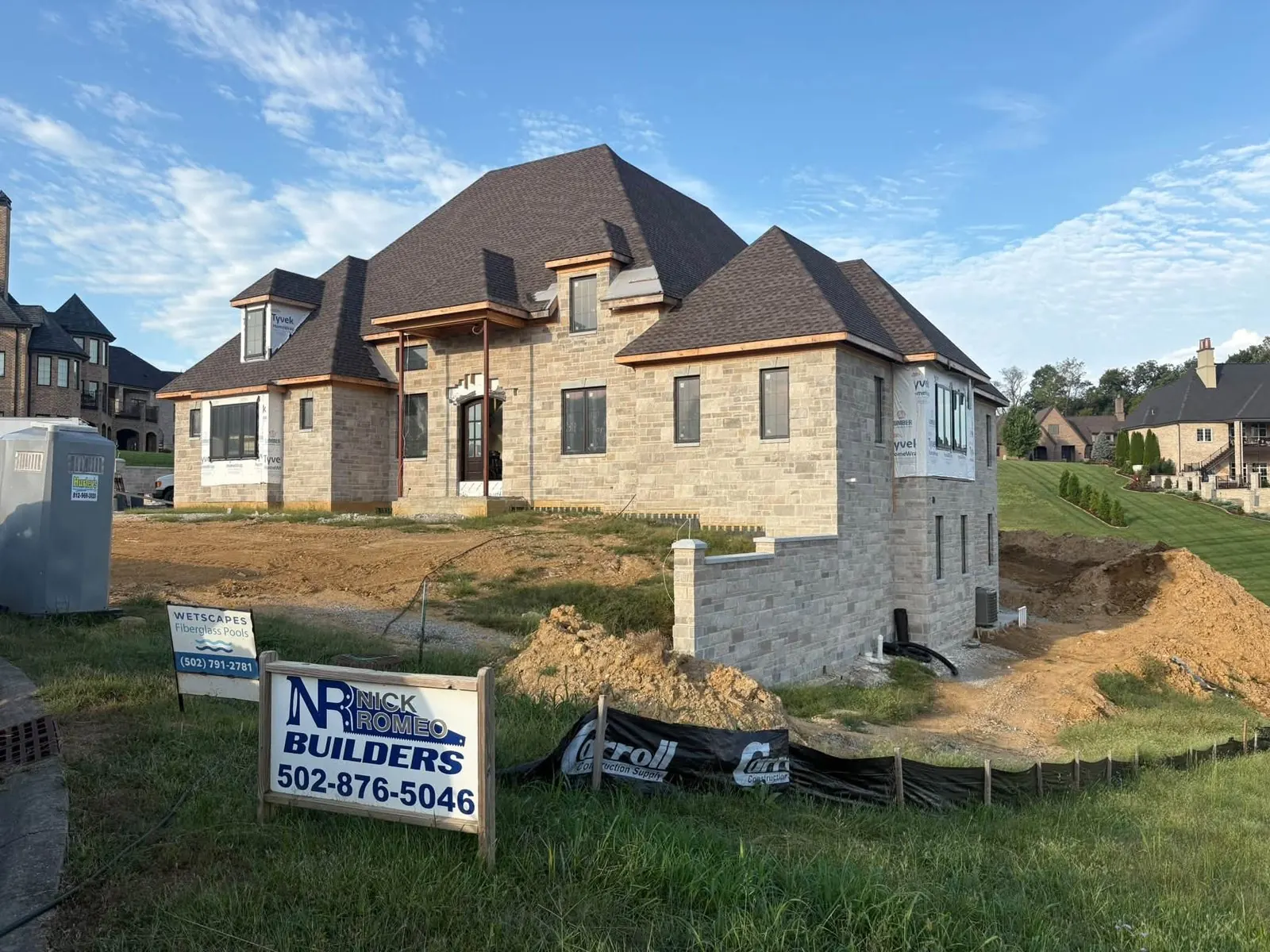 New stone house with a steep dark roof on a freshly graded lot