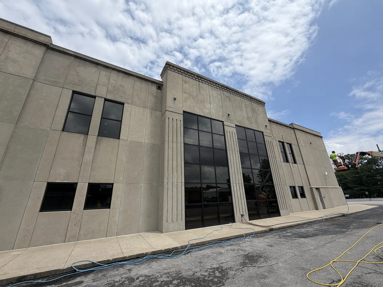 Hoses across a parking lot beside a large tan precast-concrete building during a building wash