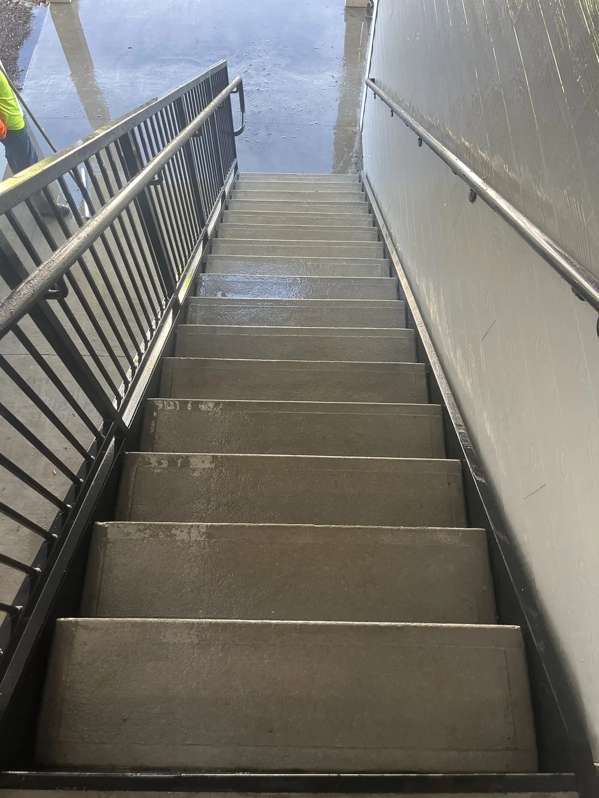 Clean, wet concrete steps in a narrow exterior stairwell with metal railings