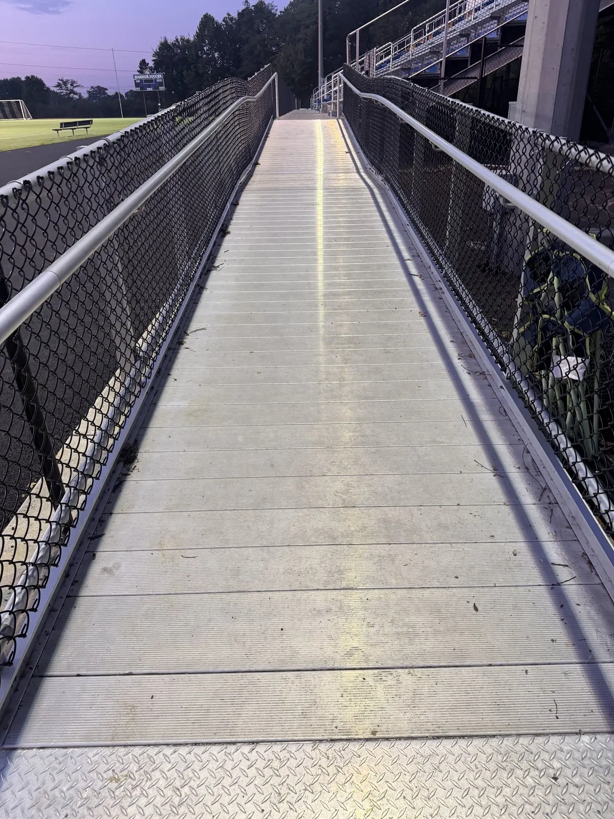 Aluminum stadium access ramp between chain-link railings at dusk