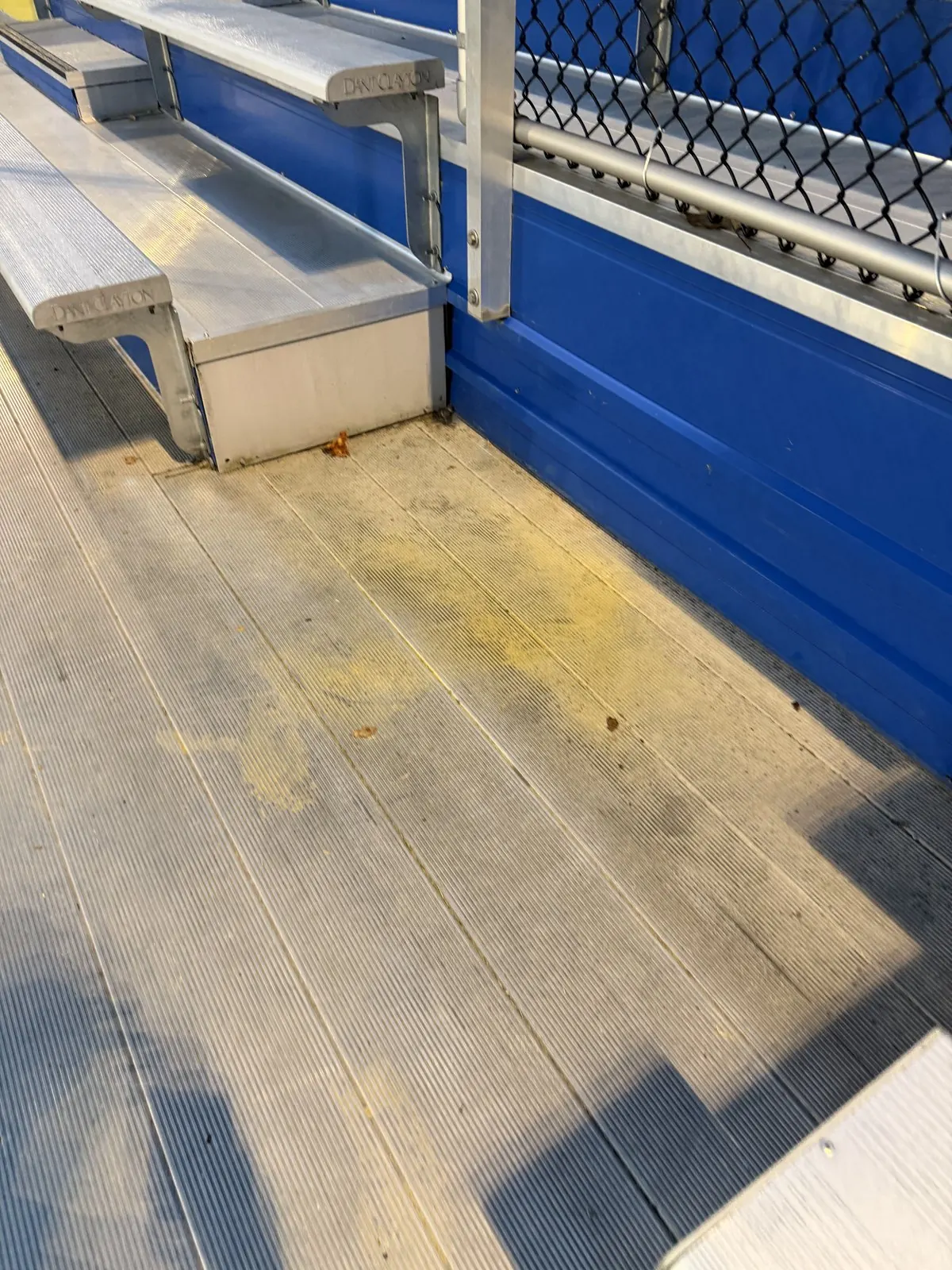 Aluminum bleacher floor with yellow and gray stains beside a blue riser wall