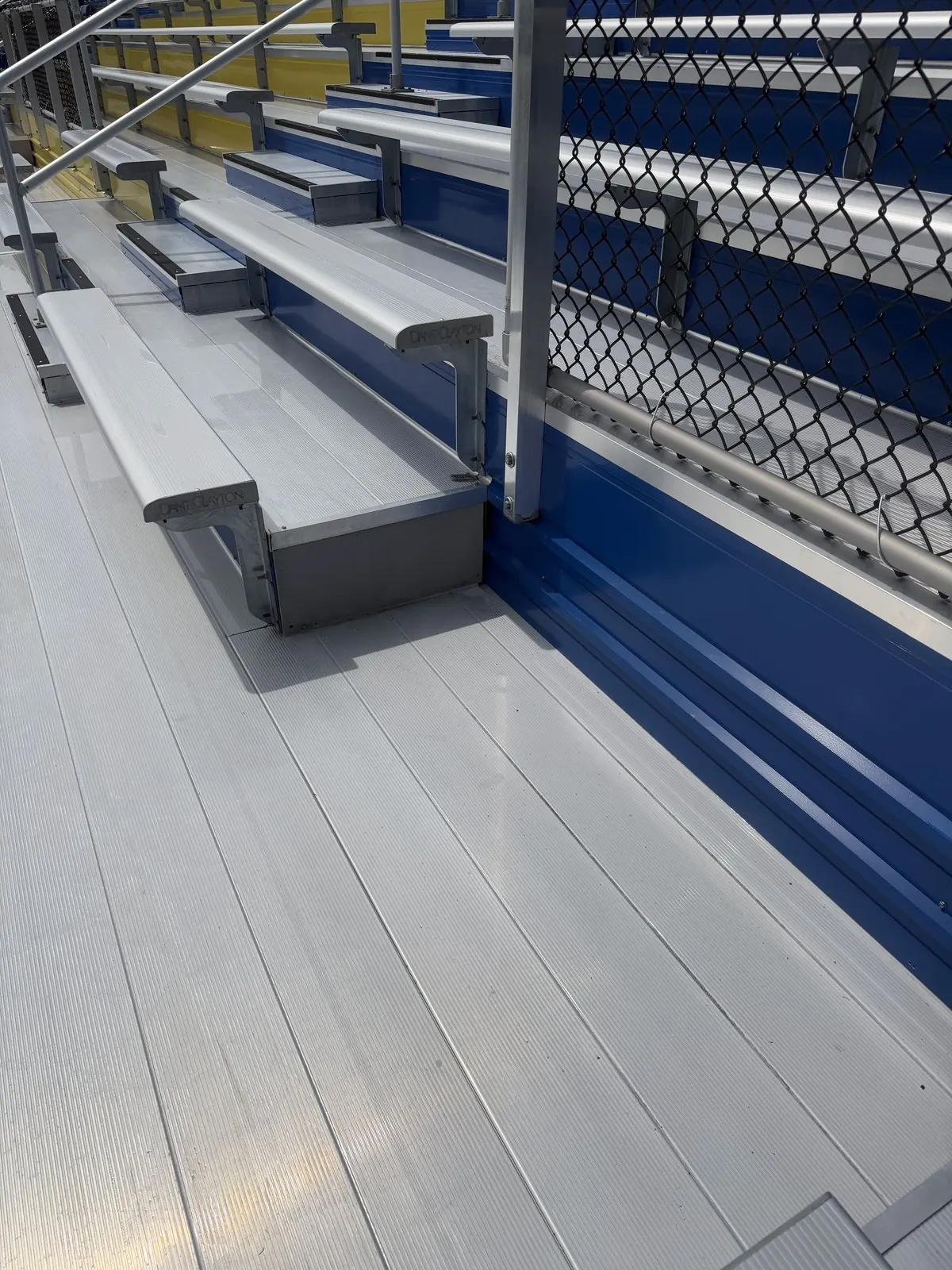 Clean aluminum bleacher seats and floor beside a blue riser wall